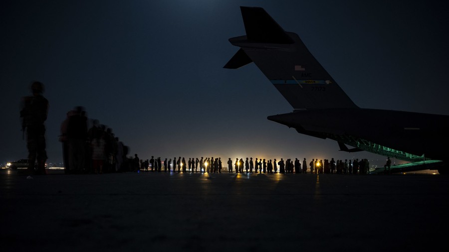 People wait in line to board a military aircraft at night.