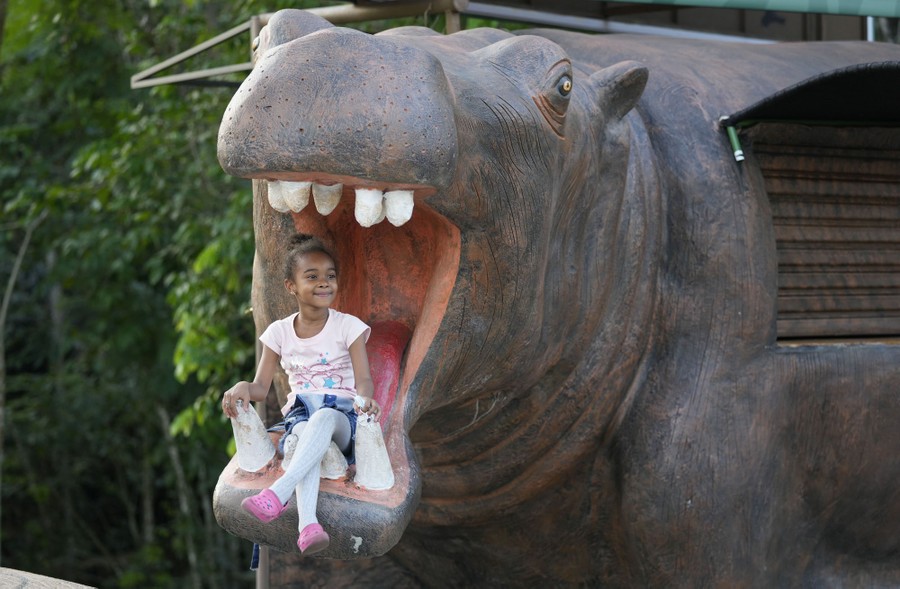 A girl sits for a photo inside the mouth of a large hippo statue.