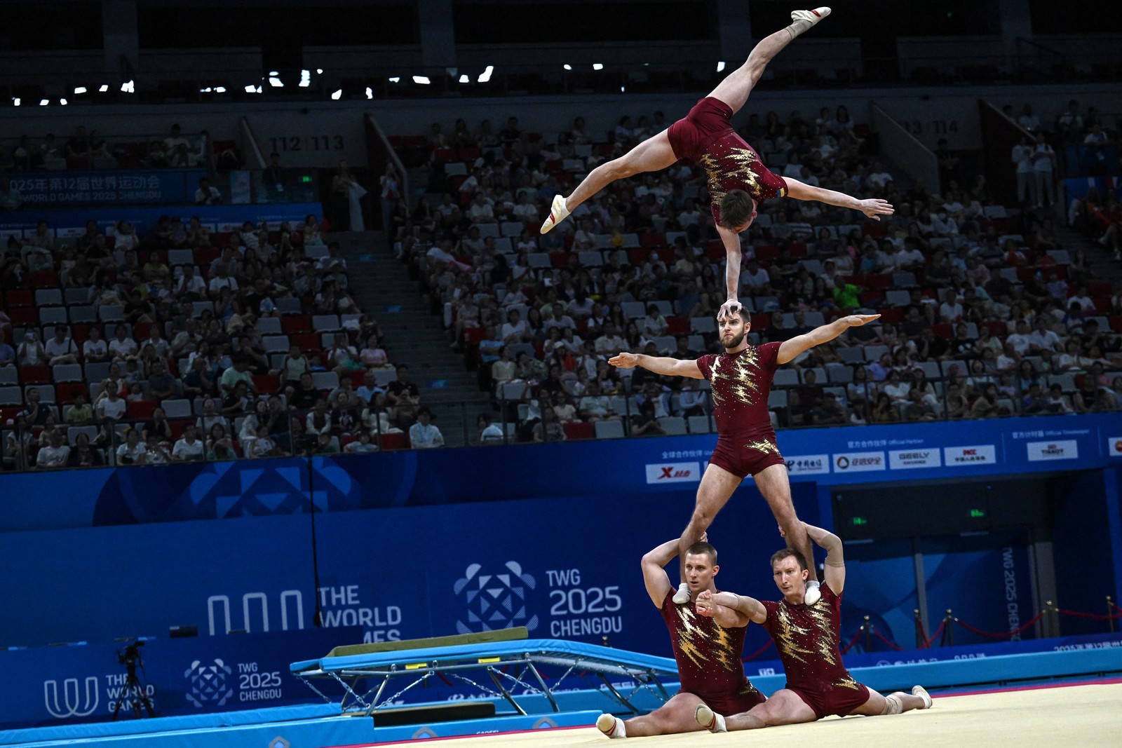 Four gymnasts pose, forming a human tower, balancing on each other's heads and shoulders.