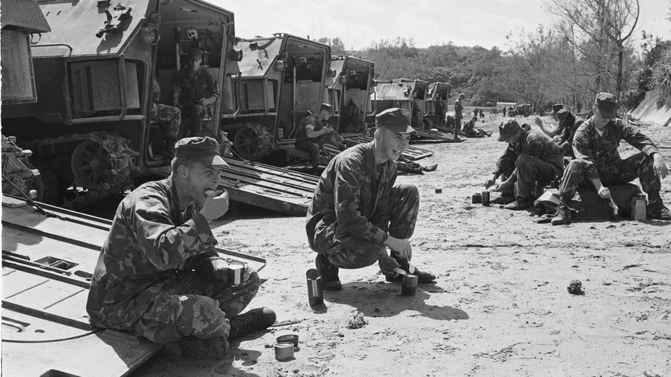 A black-and-white photo of U.S. Marines eating canned food behind a line of tanks