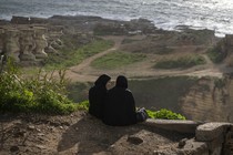 A color photograph of two women dressed in black sitting on a cliff face overlooking the water in Beirut.