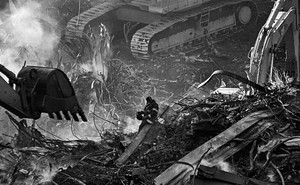 Photo of firefighter sitting on twisted metal wreckage surrounded by enormous excavators