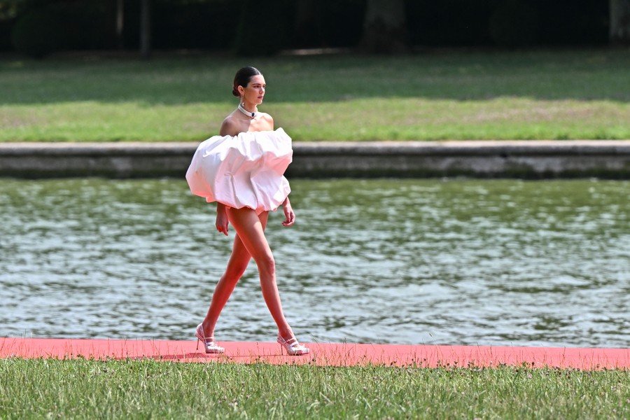 A model walks on an outdoor runway, wearing a garment bunched around their torso.