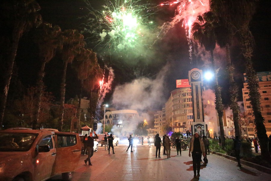 People stand in a street at night, looking at fireworks.