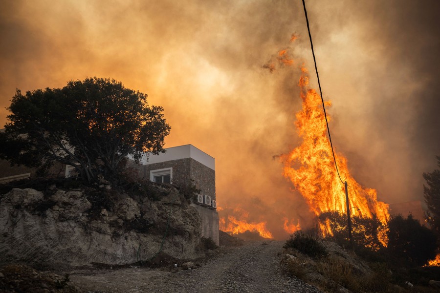 Tall flames and a smoke-filled sky are seen in a residential area on a hillside.
