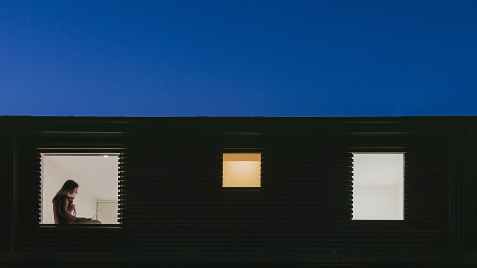 Picture of a building window showing a lonely woman using laptop