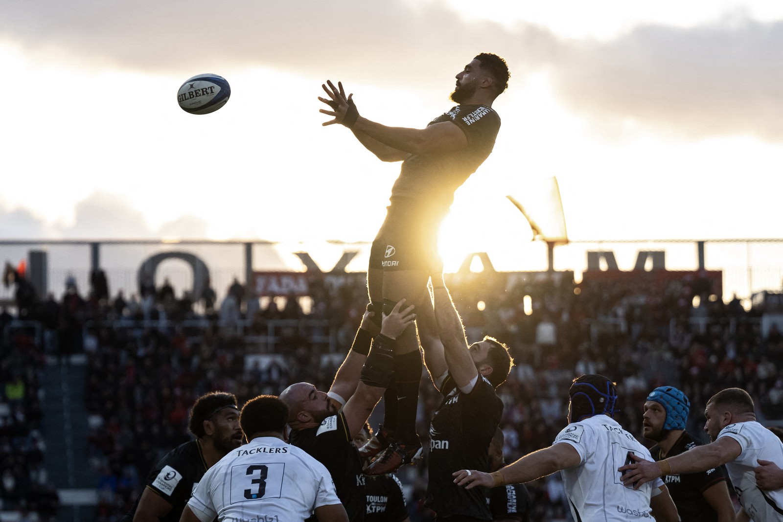 Rugby players hold a teammate high as he catches a ball.