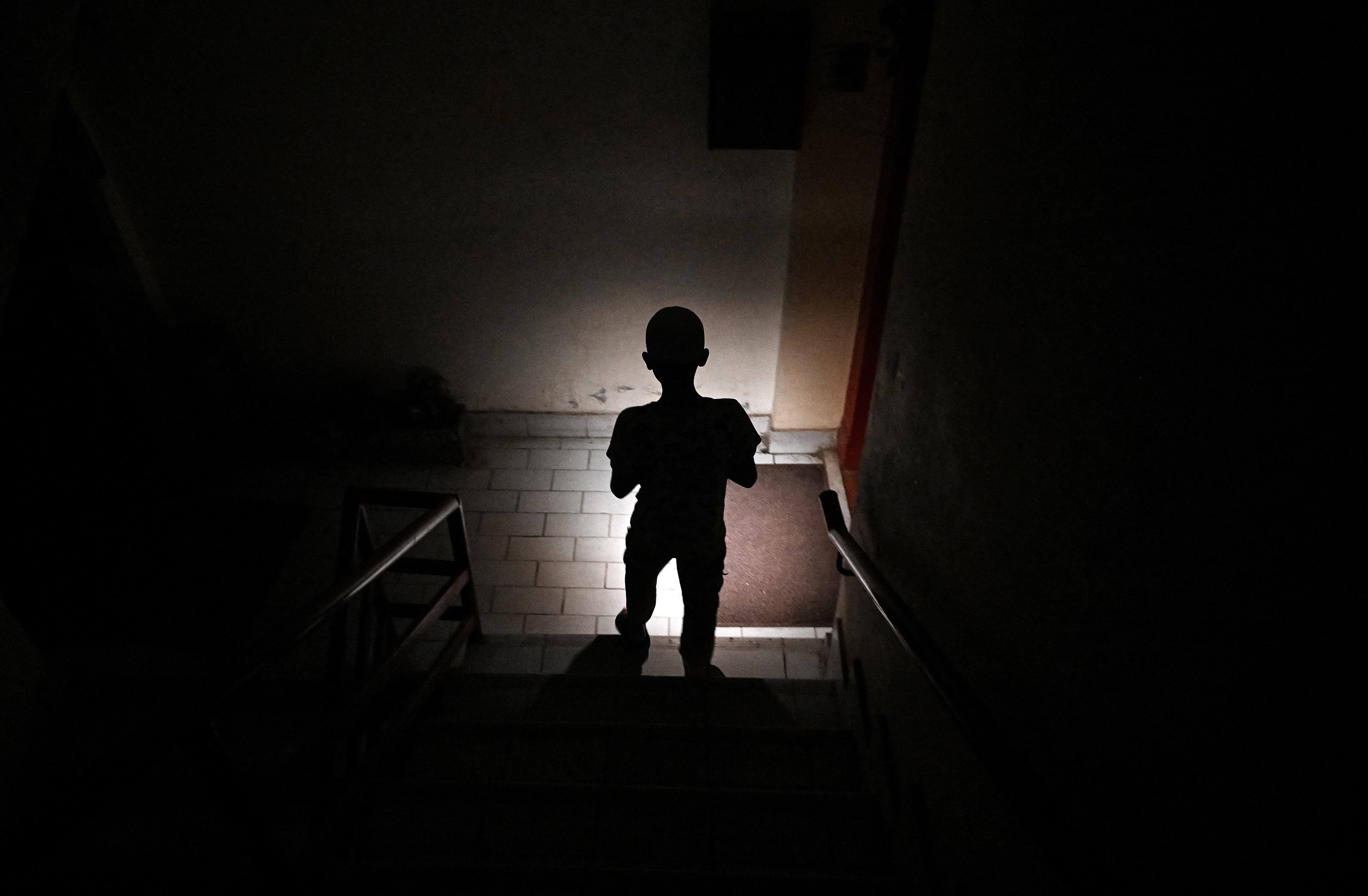 A child uses a mobile phone to light his way in a dark apartment building.