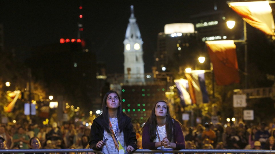 Two teens look at a television screen during Pope Francis's 2015 visit to Philadelphia.