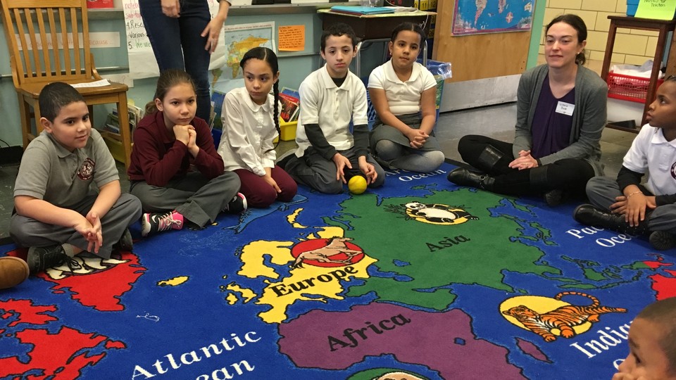 Children sit on a colorful rug decorated with a map and animals.