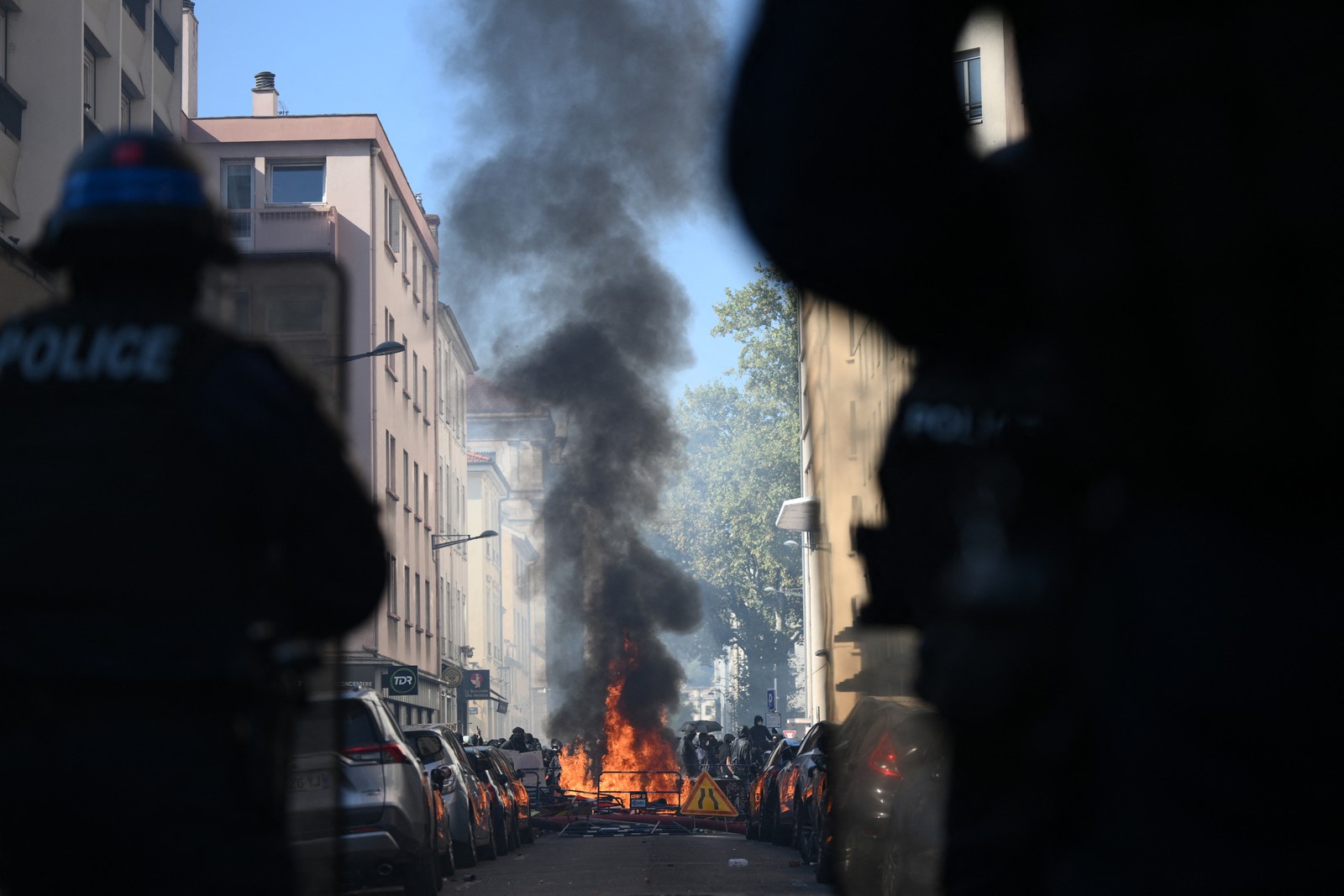 Riot police watch a fire at a makeshift barricade set up by protesters in a city street.