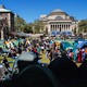 Pro-Palestinian protesters sit and stand, some in front of tents, in a large grassy area at Columbia University.