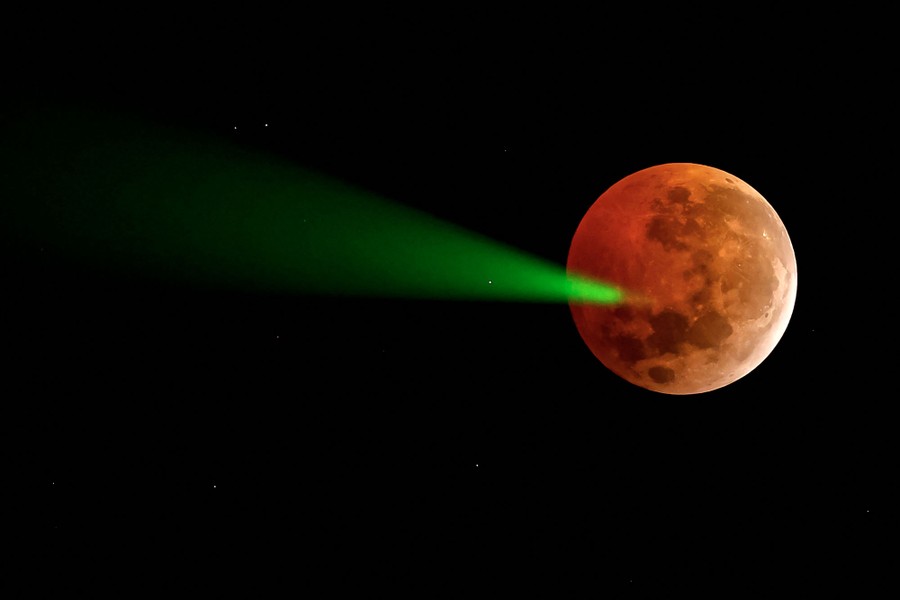 A green laser light, pointed toward the dark-red-colored moon