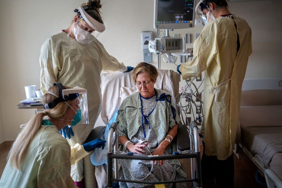 A woman sits in a hospital room surrounded by several health care workers.