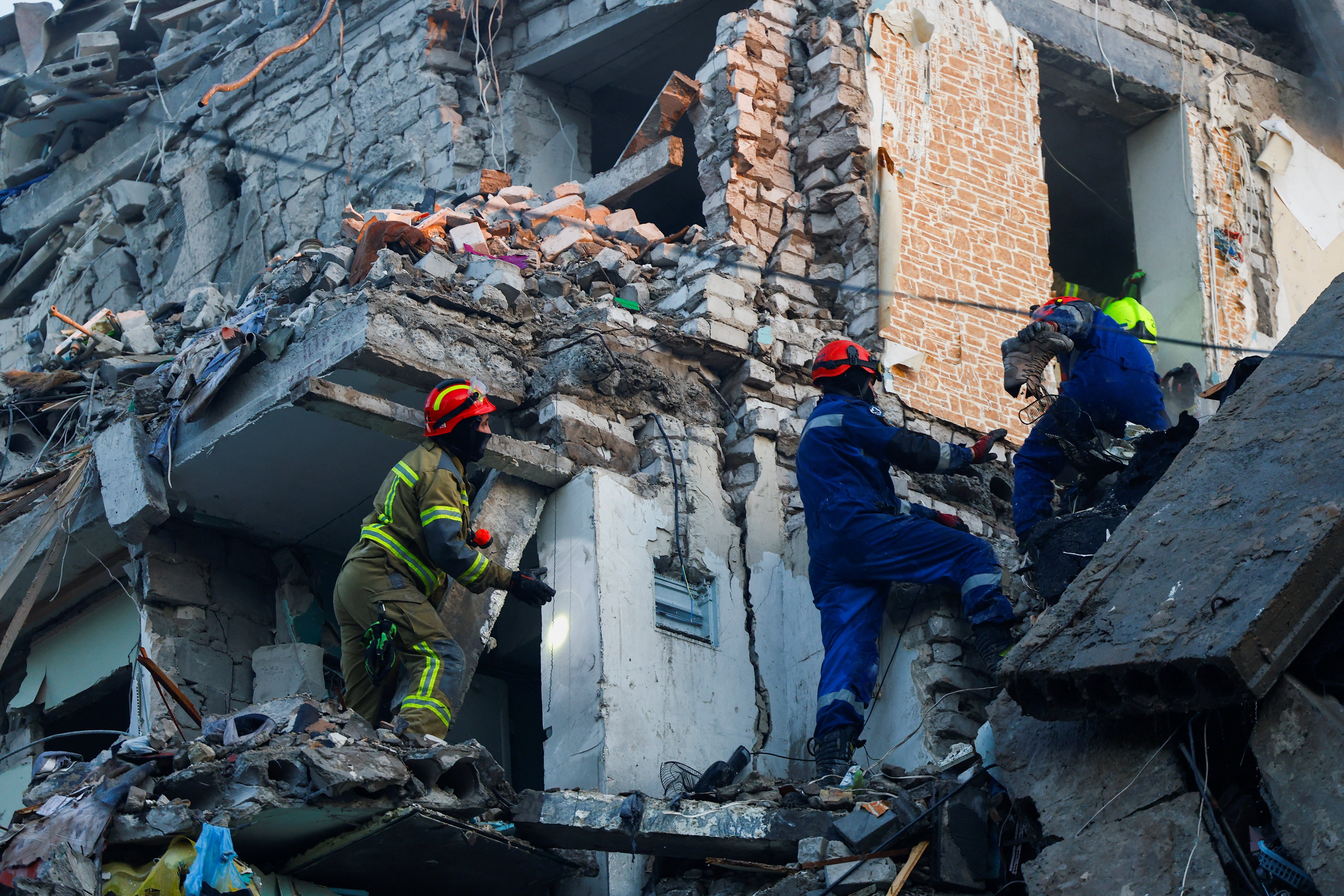 Several rescue workers climb on the ruins of a heavily damaged apartment building.