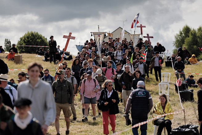 photo of large group of people walking down hill, some carrying crosses and banners, with dark clouded sky in background