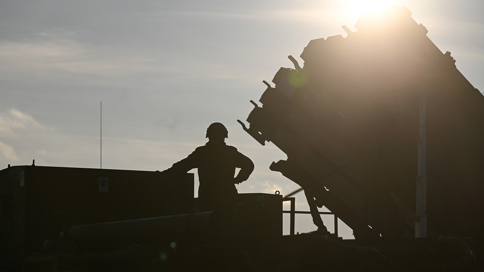 An image of a German soldier standing on top of a truck while he and others unload a US made Patriot missile.