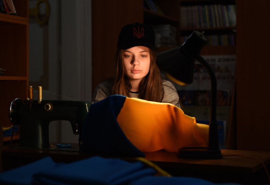 A young person works on a blue-and-yellow flag at a sewing machine.