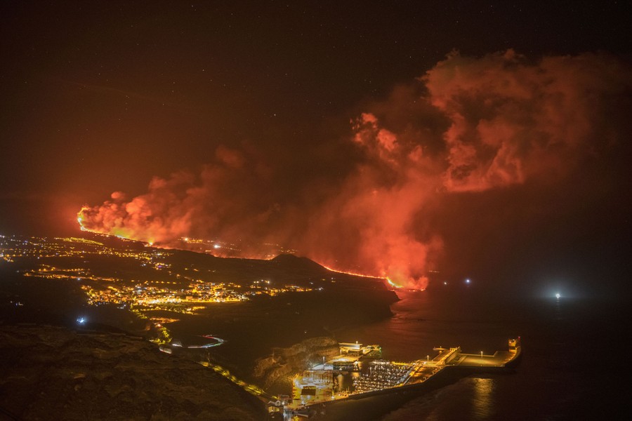 A night view of the lights of houses near a long flow of glowing lava.