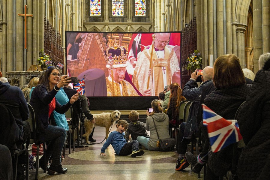 People gather inside a cathedral to watch the coronation on a big video screen.