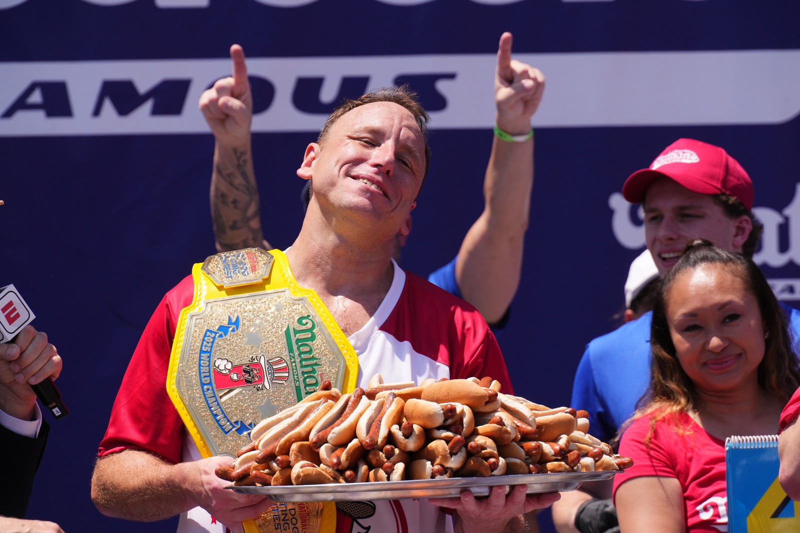 A person poses on a stage, holding a platter with dozens of hot dogs.