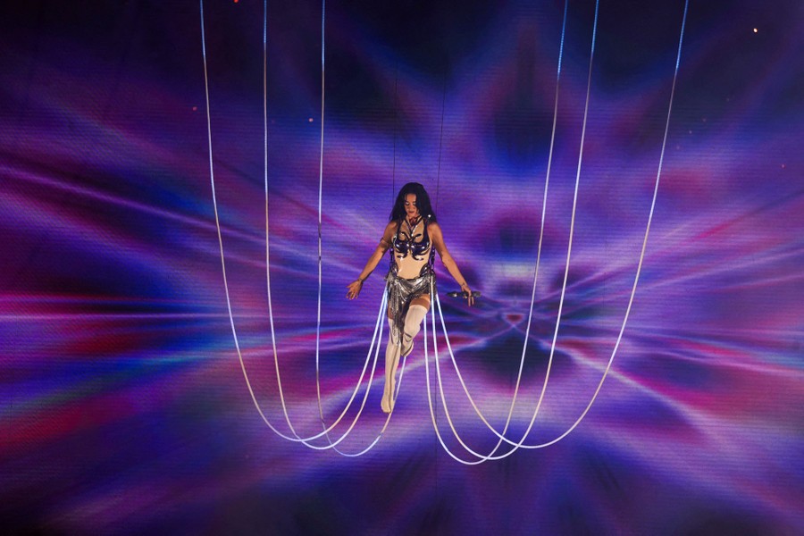 A performer hangs from wires above a stage during a concert.