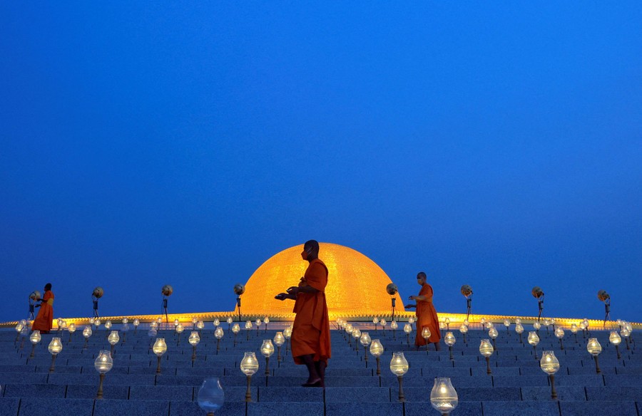 Several monks walk on a broad set of steps lighting many small lamps.