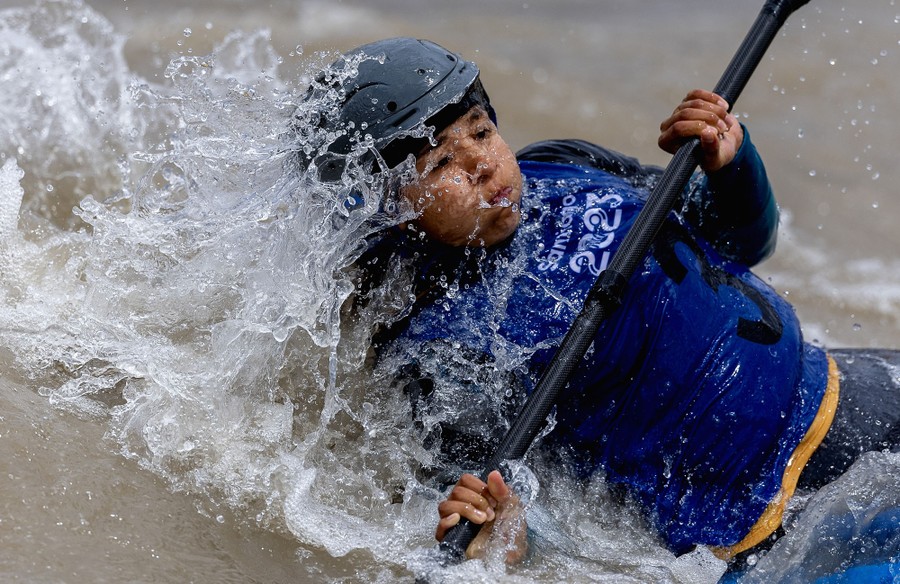 A person steers a kayak through a course, emerging from a splash of water.