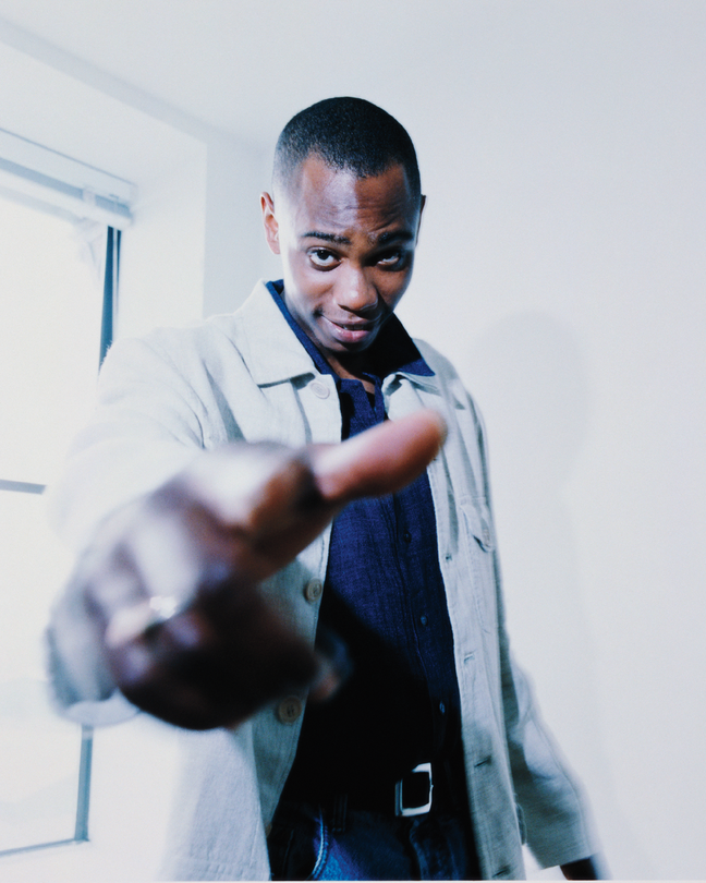 photo of Dave Chappelle next to window pointing at viewer with hand in foreground