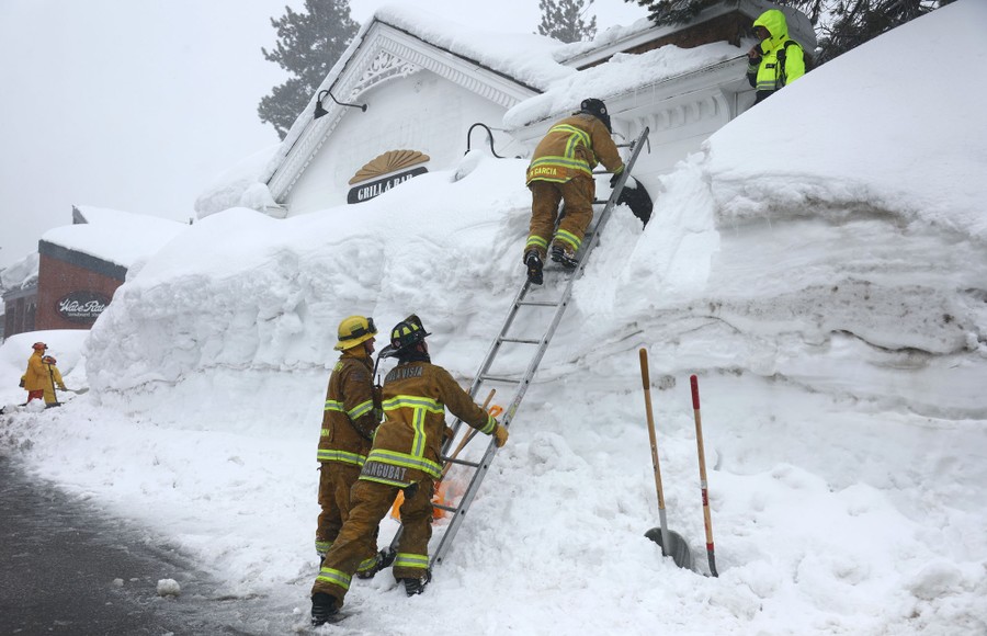 Firefighters use a ladder to scale a huge snowbank.