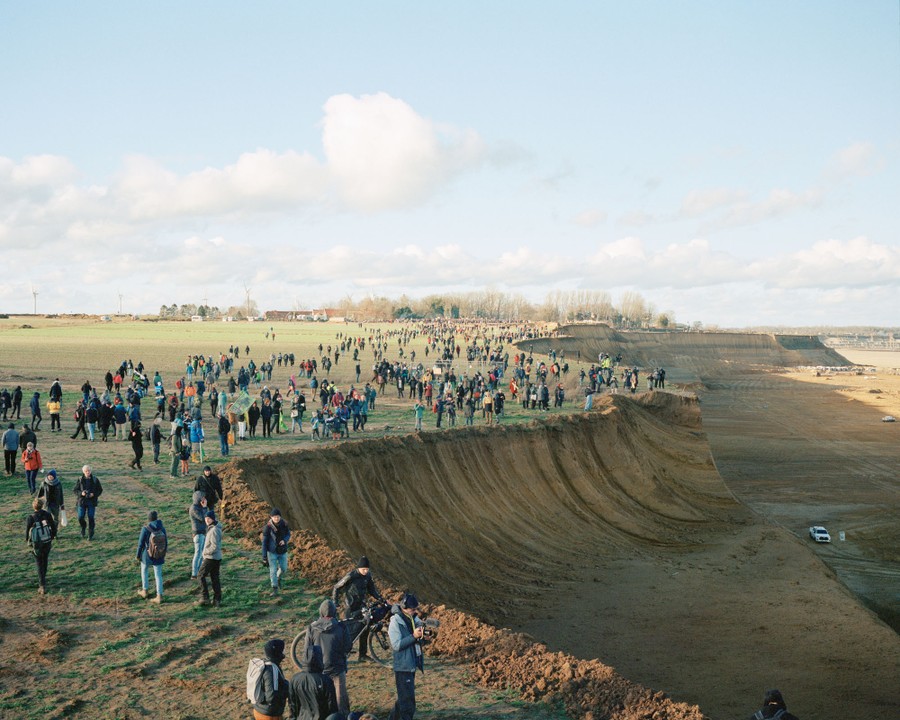 Hundreds of people walk in fields along the outside edge of an open-pit mine.