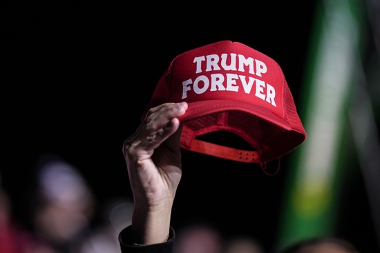 A Trump supporter holds up a red baseball cap that reads Trump Forever