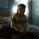 Kristen Stewart sitting on a bed with her phone in 'Personal Shopper'