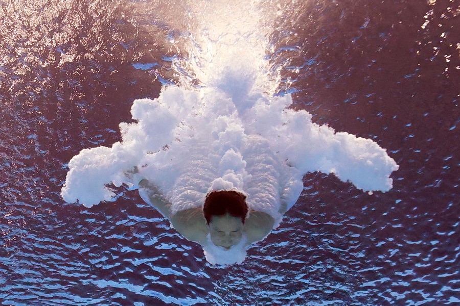 A diver splashes into a pool, captured underwater, creating a cloud of bubbles.