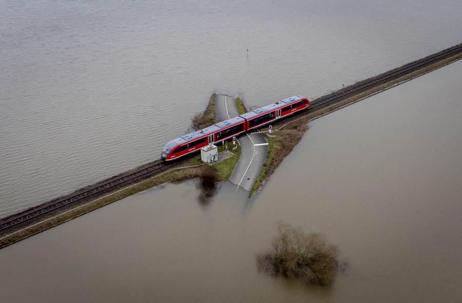 A train passes over a slightly raised railroad crossing between flooded fields.