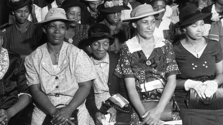 A black-and-white image of Black women sitting in church pews