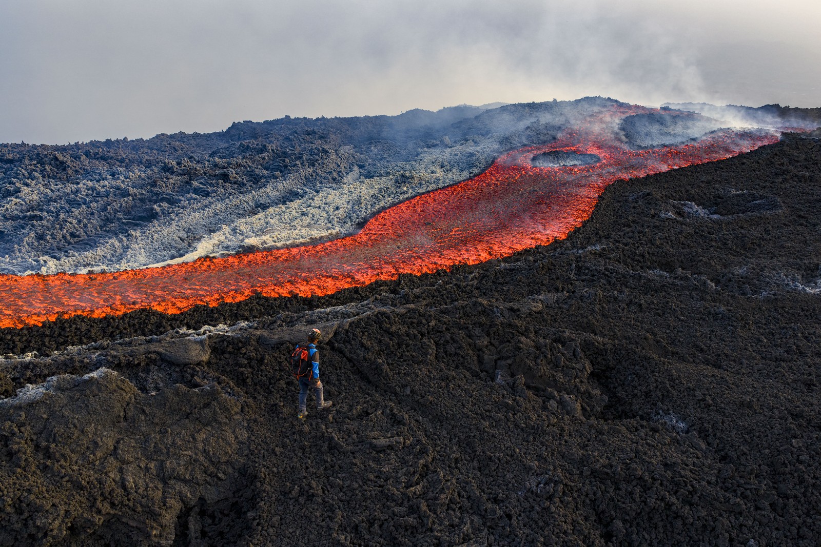 A person walks on solidified lava, past flowing hot lava