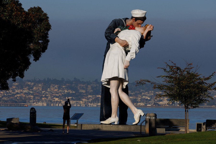 A jogger takes a photo of a large sculpture of a WWII-era sailor embracing and kissing a nurse.