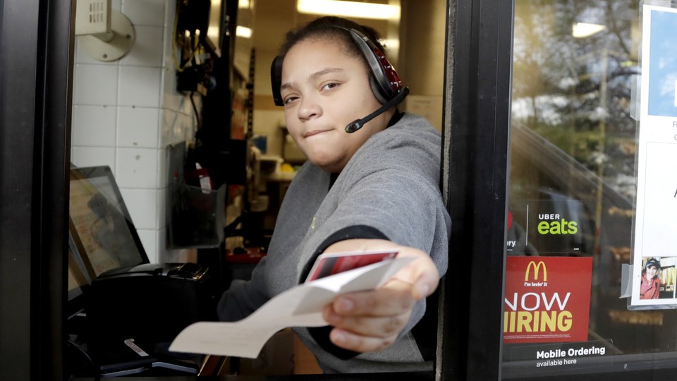 A McDonald's worker at a drive-through hands someone behind the camera a receipt.