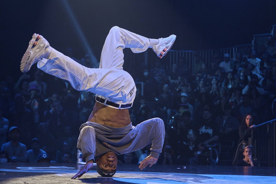 A dancer performs an acrobatic move in front of a crowd, while upside down, supported by only their head.