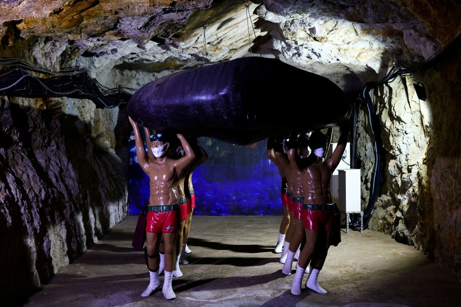 Eight mannequins hold up an inflatable raft inside a cave.