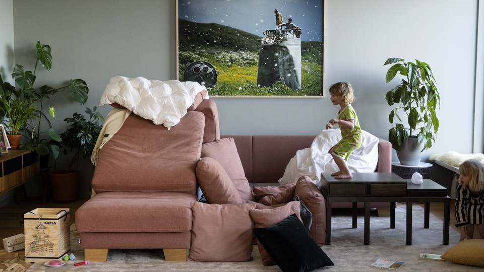 A child stands on a table, staring at a recently-made pillow fort.