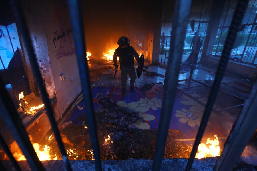 Riot police officers walk through a damaged, partially burning building.