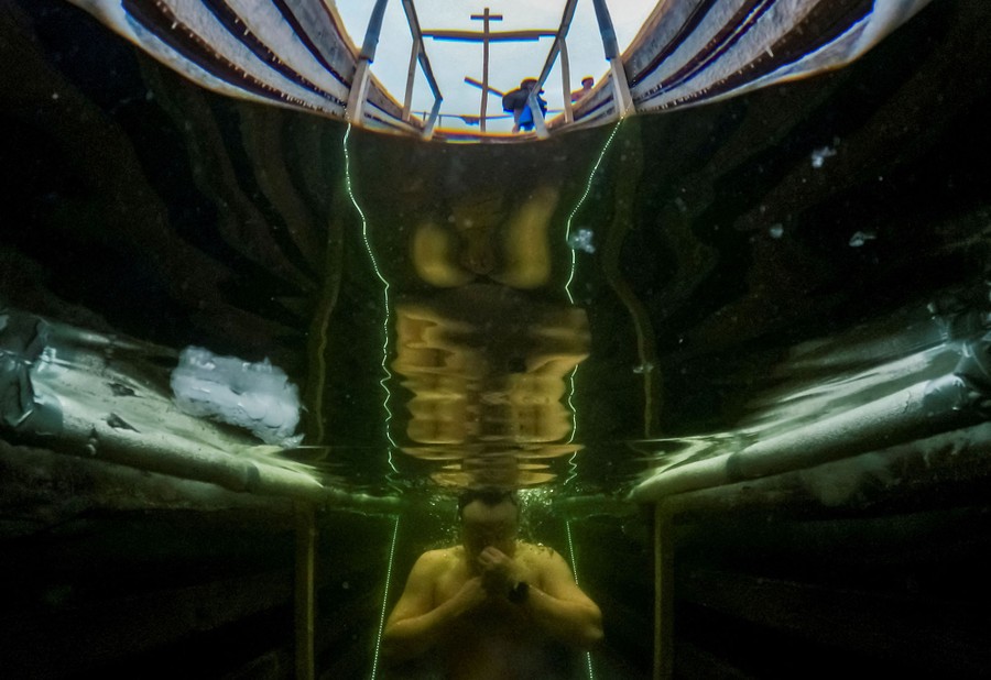 An underwater view of a person taking a dip in water accessed through a hole cut in ice