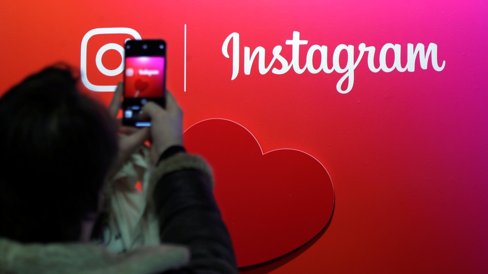 A person uses their cellphone to take a photo of the Instagram logo.