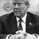 Black-and-white photo of Donald Trump in a suit siting with his hands crossed in front of him