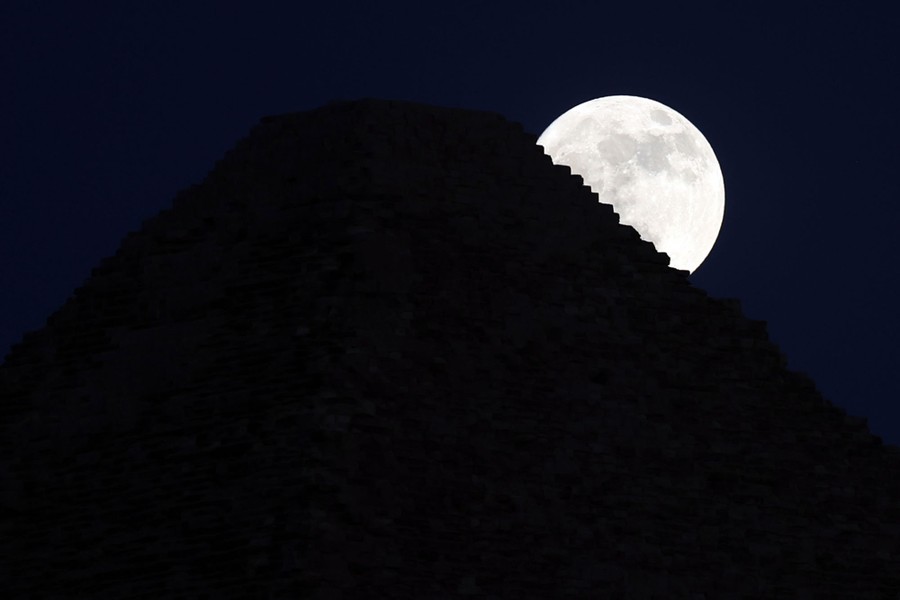 A view of the full moon behind an Egyptian pyramid