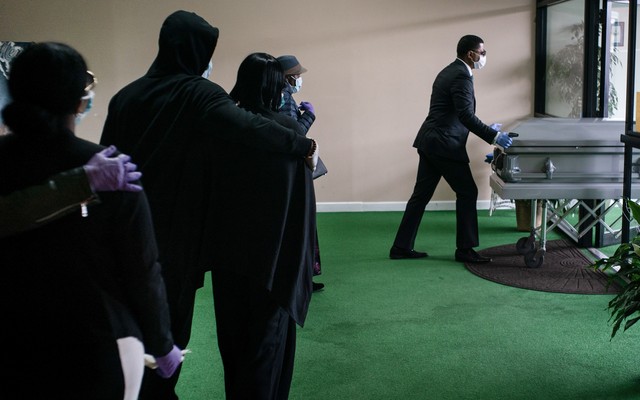 A funeral procession in New Jersey. A black man wearing a mask is pushing a casket.