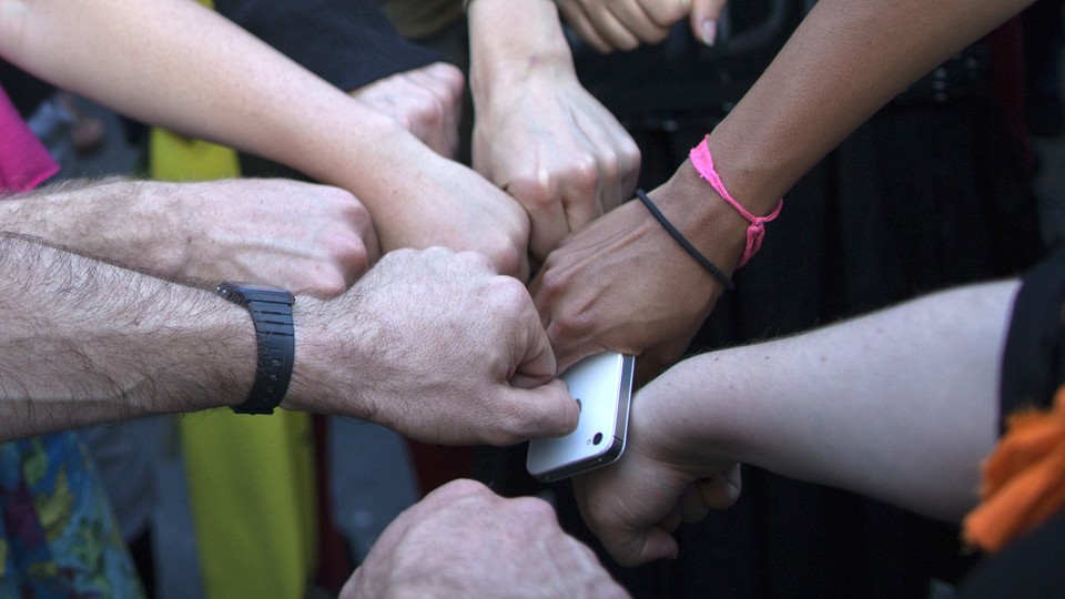 Activists join fists in solidarity ahead of a protest march, with one holding an iPhone
