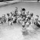Children listen to a battery-powered radio receiver that is set on a table in a swimming pool.